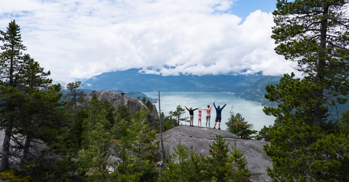 A family enjoy the views after a budget-friendly hike to the top of the mountain. They are on top of a mountain admiring the view during their Canadian travel.