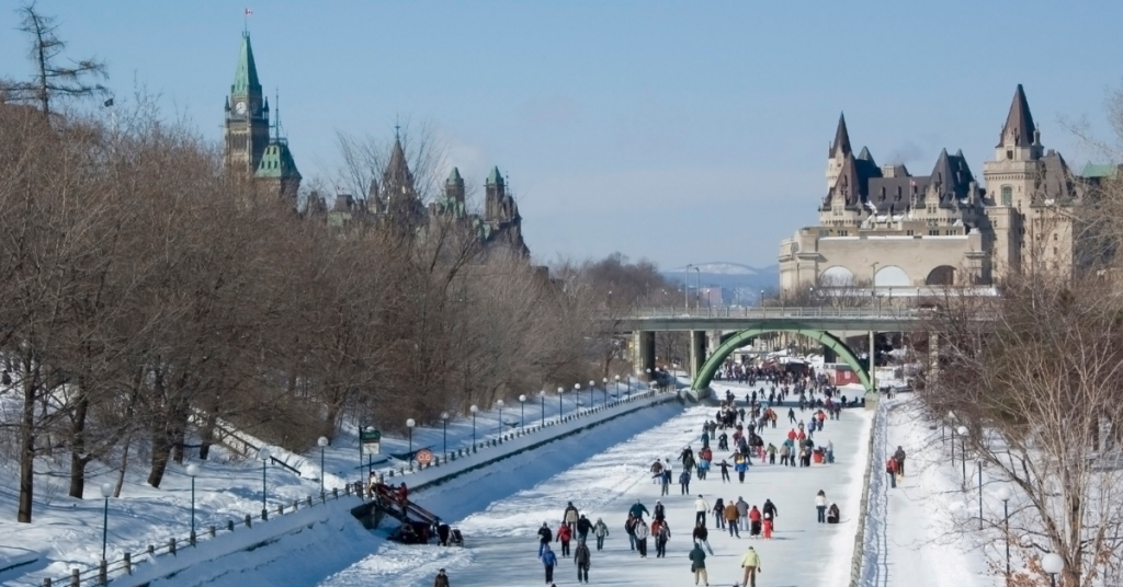 Winter activity scene of people ice skating on the frozen Rideau Canal with the picturesque backdrop of Ottawa’s historic buildings and skyline, capturing the joy of this popular Canadian winter pastime and the beauty of the capital city.