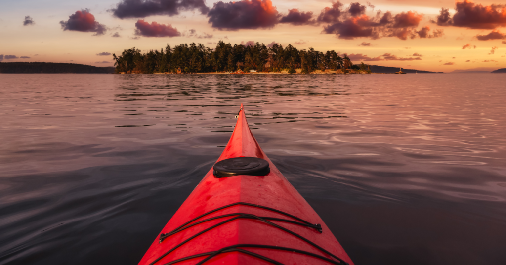 Serene kayaking experience at sunset in the Pacific Rim National Park Reserve with a first-person perspective from a red kayak gliding over calm waters, highlighting the tranquil and scenic adventure opportunities in this Canadian coastal park.