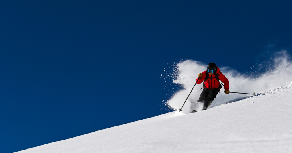 Dynamic action shot of a skier dressed in bright red descending a steep slope with fresh powder snow flying around in Whistler, Canada, emphasizing the thrill and excitement of skiing in one of the world's top winter sports destinations.